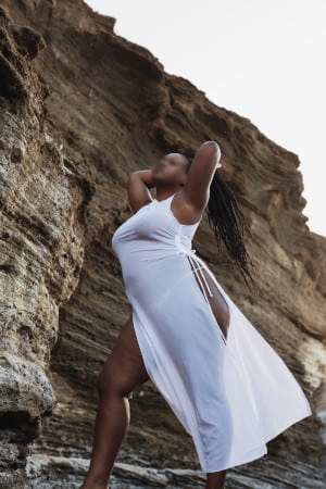 Dramatic photo of a curvy black woman in a white dress by the foot of a rocky mountain